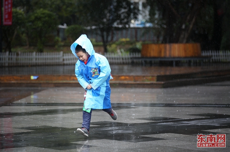 一位刚放学的学生穿着雨衣在雨中奔跑躲雨