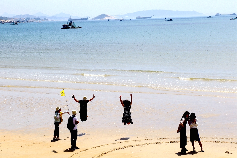 游客在纯净的沙滩上欢快地奔跑、跳跃着.jpg